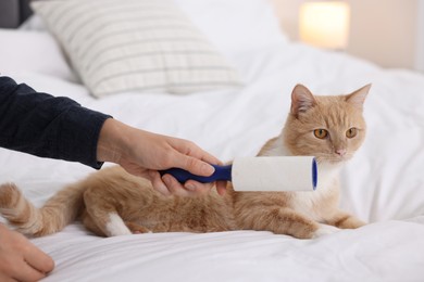 Photo of Woman with lint roller and her cat on bed at home, closeup