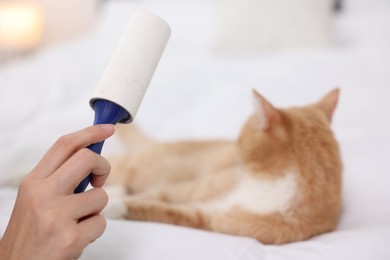 Photo of Woman with lint roller and her cat on bed, selective focus