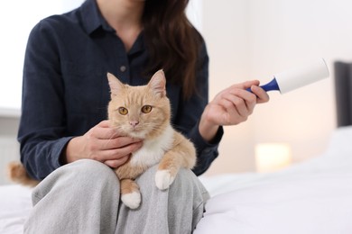 Photo of Woman with lint roller and her cat on bed at home, closeup