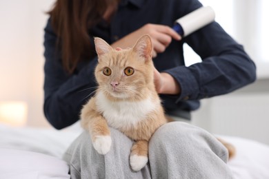 Photo of Woman with lint roller removing pet's hair from clothes and her cat on bed at home, closeup