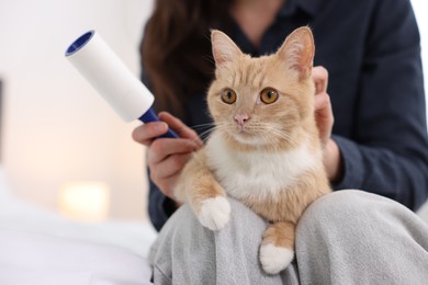Photo of Woman with lint roller and her cat on bed at home, closeup. Space for text