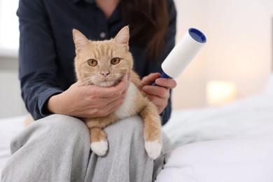 Photo of Woman with lint roller and her cat on bed at home, closeup. Space for text