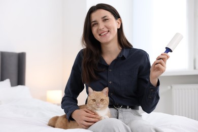 Photo of Smiling woman with lint roller and her cat on bed at home