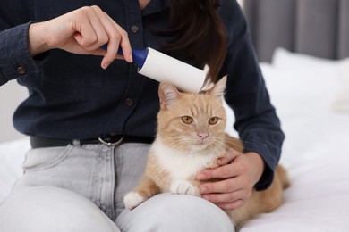 Photo of Woman rubbing down her cat with lint roller on bed, closeup