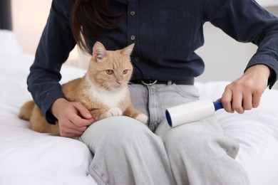 Photo of Woman with lint roller removing pet's hair from clothes and her cat on bed at home, closeup