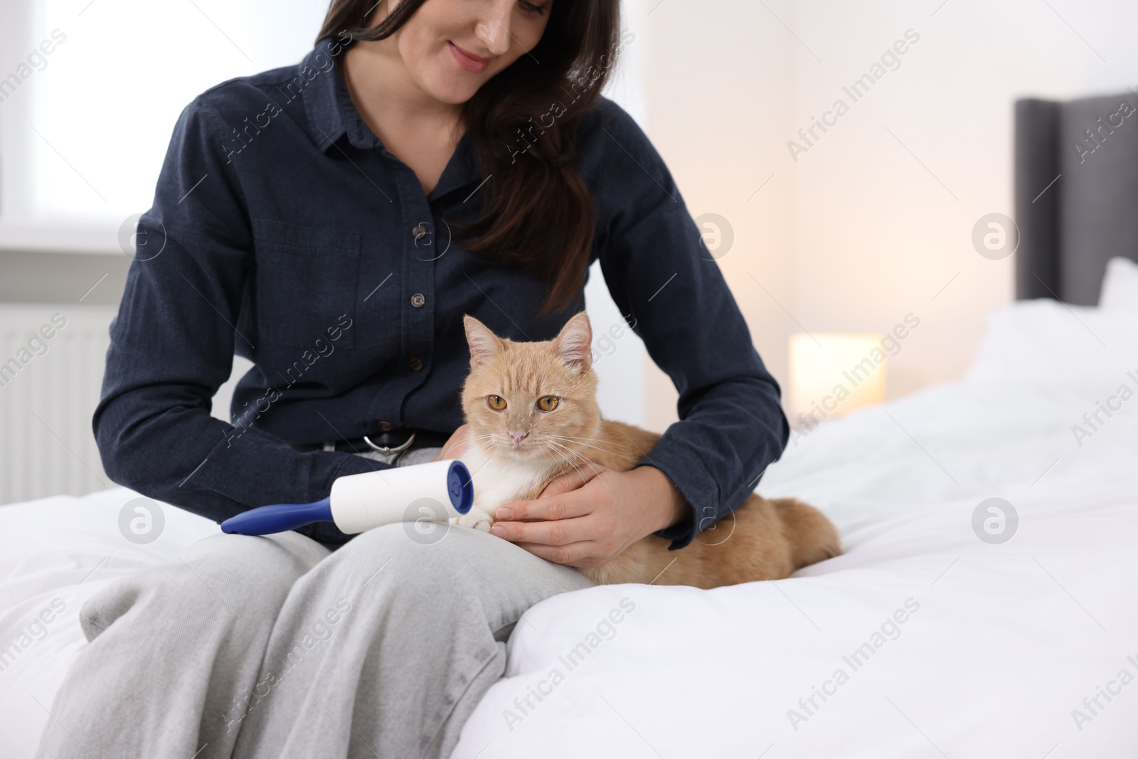 Photo of Woman with lint roller and her cat on bed at home, closeup. Space for text