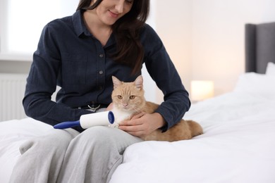 Photo of Woman with lint roller and her cat on bed at home, closeup. Space for text