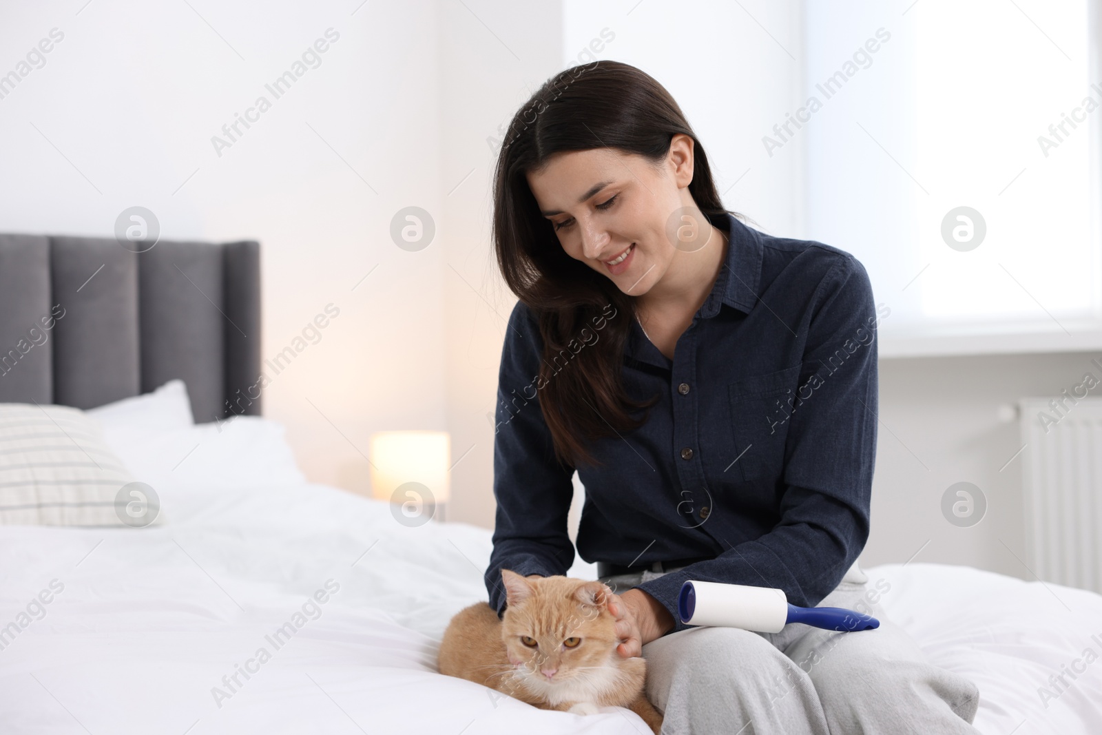 Photo of Smiling woman with lint roller stroking her cat on bed at home. Space for text