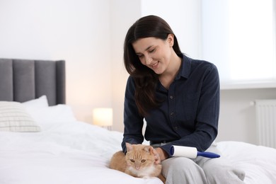Photo of Smiling woman with lint roller stroking her cat on bed at home. Space for text
