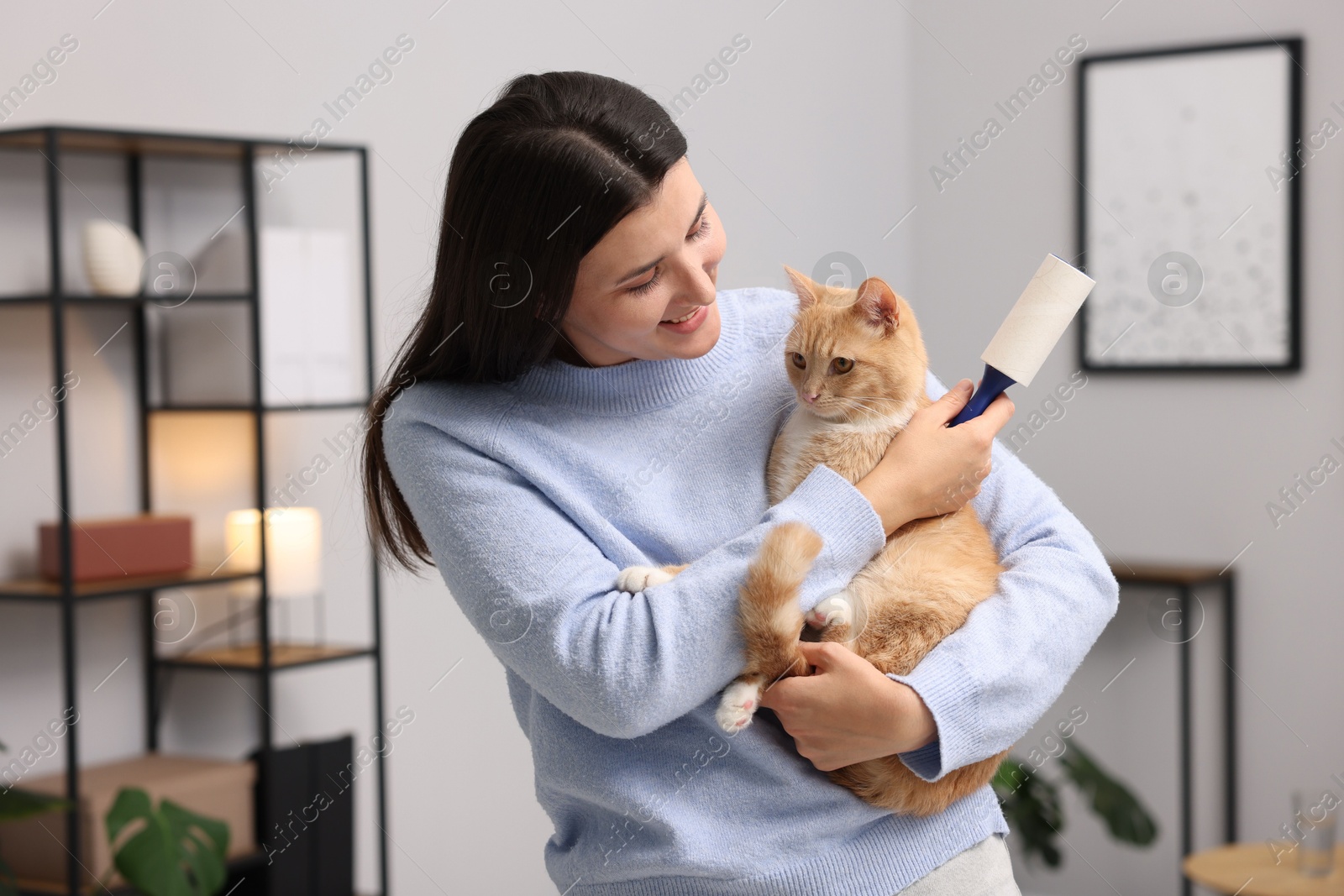 Photo of Smiling woman with lint roller and her cat at home