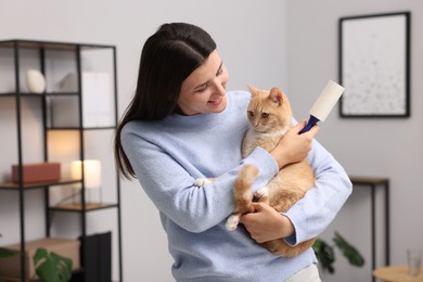 Photo of Smiling woman with lint roller and her cat at home