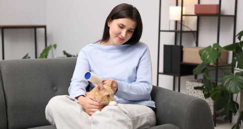 Photo of Woman with lint roller and her cat on sofa at home