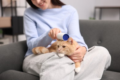 Photo of Smiling woman rubbing down her cat with lint roller on sofa, closeup
