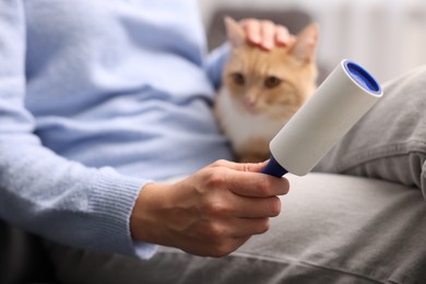 Photo of Woman with lint roller stroking her cat at home, selective focus