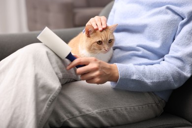 Photo of Woman with lint roller removing pet's hair from clothes and her cat on sofa at home, closeup
