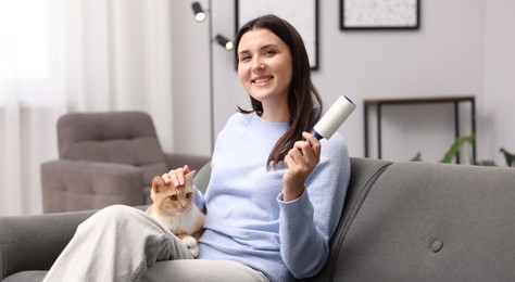 Photo of Smiling woman with lint roller stroking her cat on sofa at home