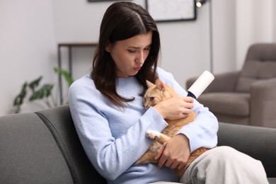 Photo of Woman with lint roller and her cat on sofa at home