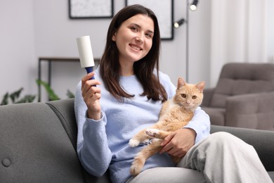 Photo of Smiling woman with lint roller and her cat on sofa at home