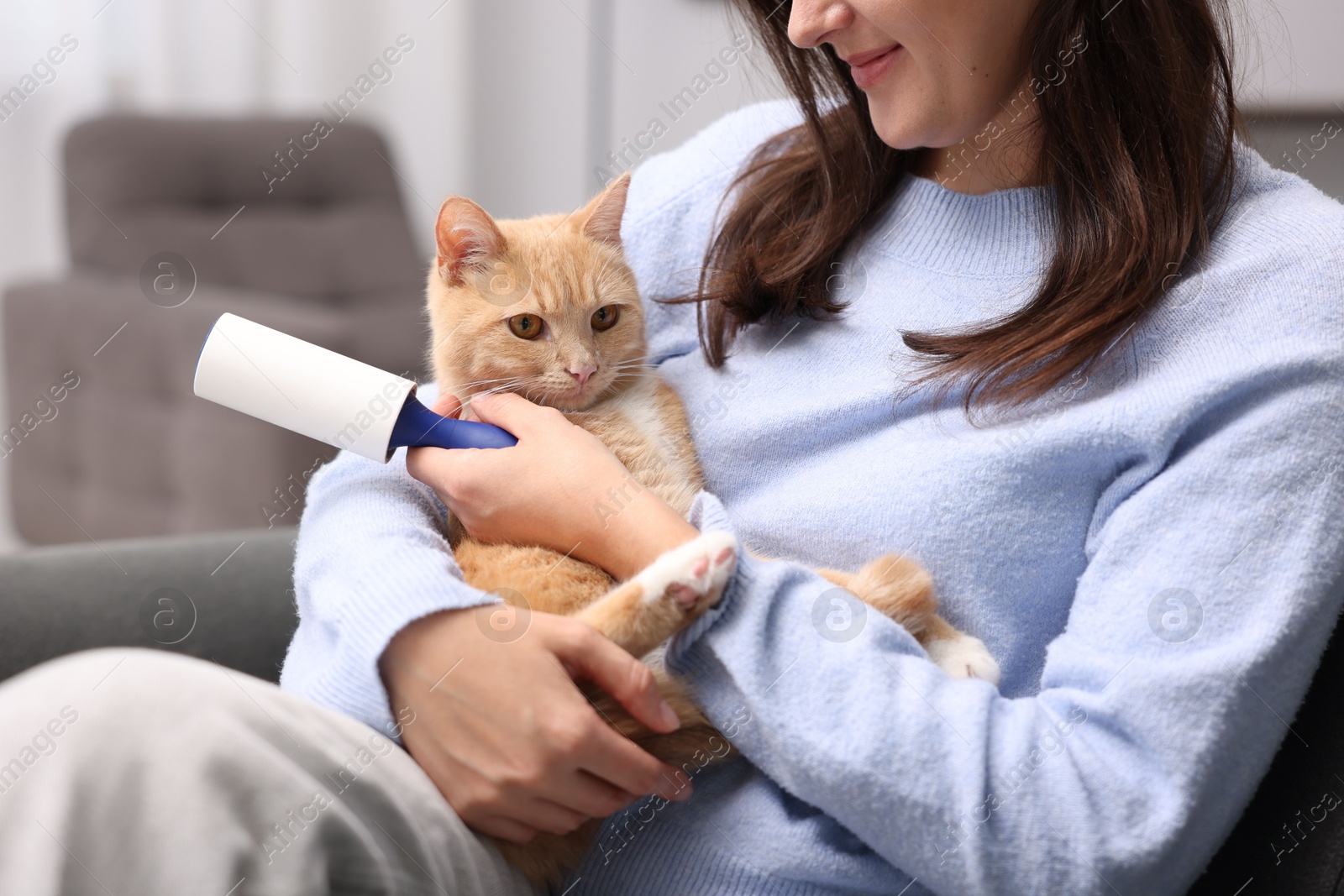 Photo of Woman with lint roller and her cat on sofa at home, closeup
