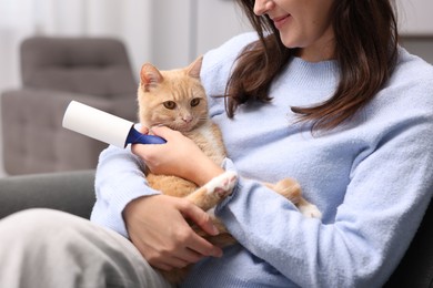 Photo of Woman with lint roller and her cat on sofa at home, closeup