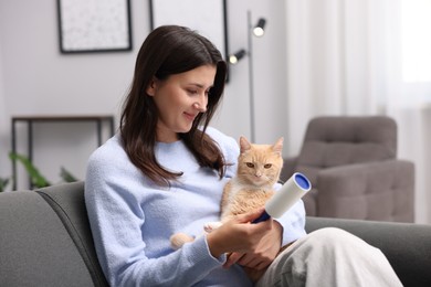 Photo of Smiling woman with lint roller and her cat on sofa at home