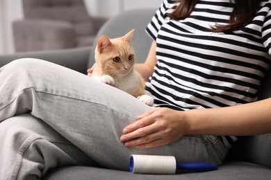Photo of Woman with lint roller and her cat on sofa at home, closeup