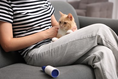 Photo of Woman with lint roller and her cat on sofa at home, closeup