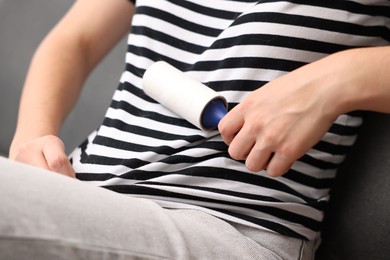 Photo of Woman with lint roller removing pet's hair from clothes on sofa, closeup