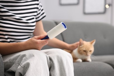 Photo of Woman with lint roller stroking her cat on sofa at home, closeup