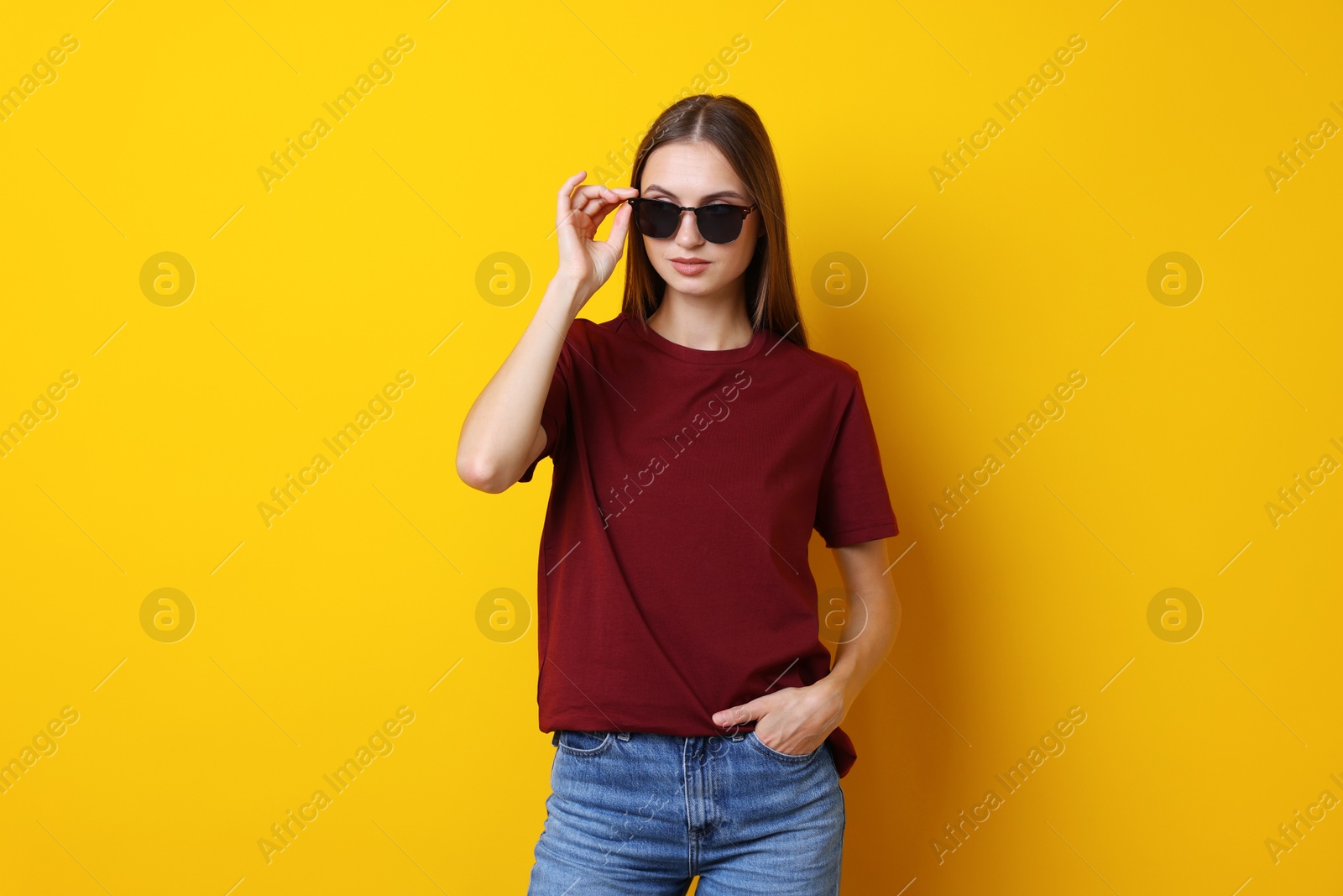 Photo of Woman wearing stylish burgundy t-shirt and sunglasses on yellow background