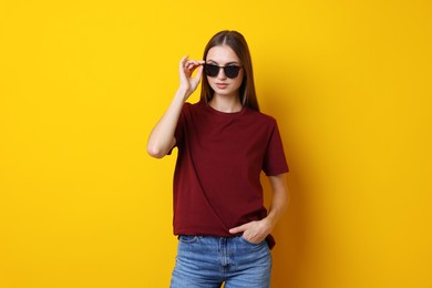 Photo of Woman wearing stylish burgundy t-shirt and sunglasses on yellow background