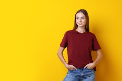 Photo of Woman wearing stylish burgundy t-shirt on yellow background. Space for text
