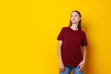 Photo of Woman wearing stylish burgundy t-shirt on yellow background. Space for text