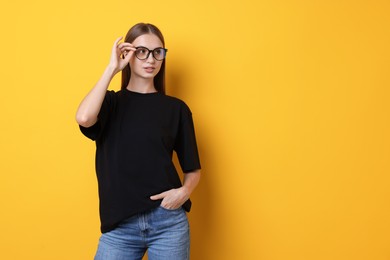 Photo of Woman wearing stylish black t-shirt on yellow background. Space for text