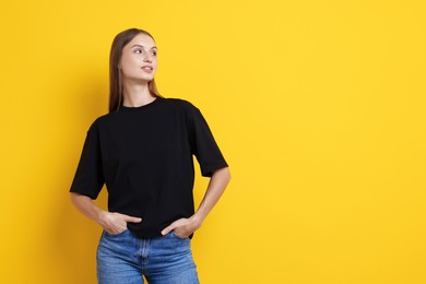 Photo of Woman wearing stylish black t-shirt on yellow background. Space for text