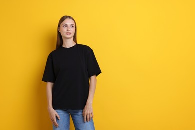 Photo of Woman wearing stylish black t-shirt on yellow background. Space for text