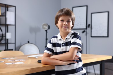 Photo of Choice of profession. Little boy pretending to be photographer leaning on wooden table with pictures in studio