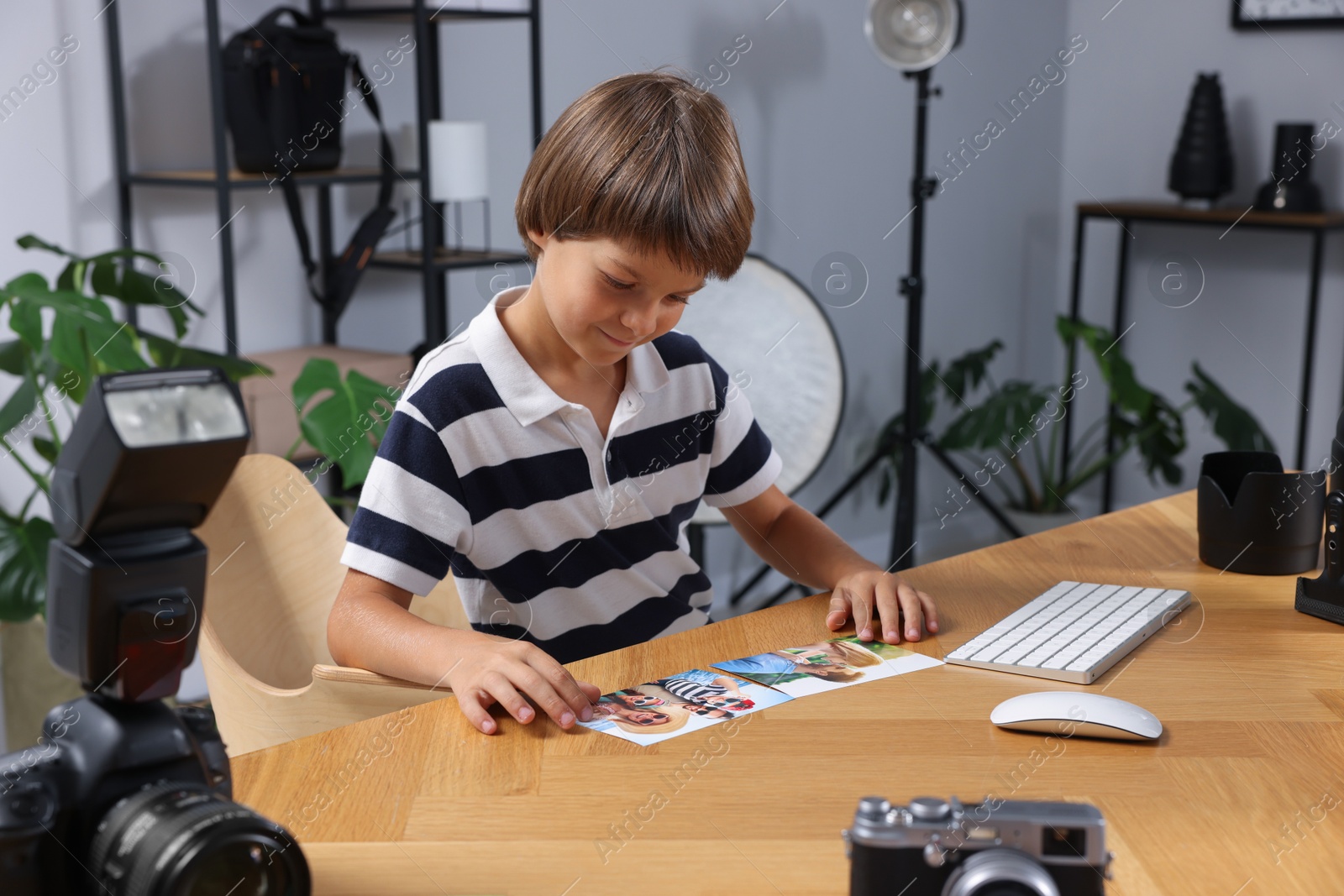 Photo of Choice of profession. Little boy with pictures pretending to be photographer at wooden table in studio