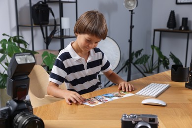 Photo of Choice of profession. Little boy with pictures pretending to be photographer at wooden table in studio