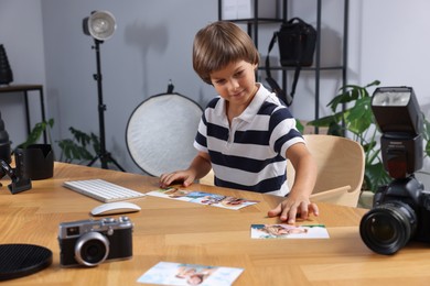 Photo of Choice of profession. Little boy with pictures pretending to be photographer at wooden table in studio
