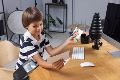 Photo of Choice of profession. Little boy with pictures pretending to be photographer at wooden table in studio