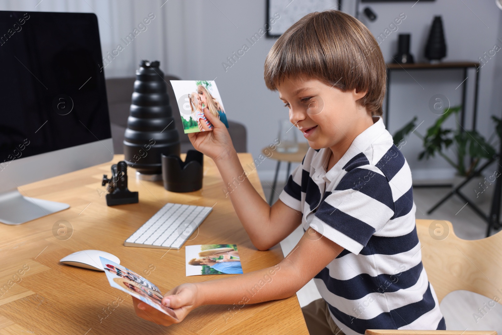 Photo of Choice of profession. Little boy with pictures pretending to be photographer at wooden table in studio