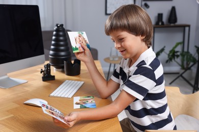 Photo of Choice of profession. Little boy with pictures pretending to be photographer at wooden table in studio