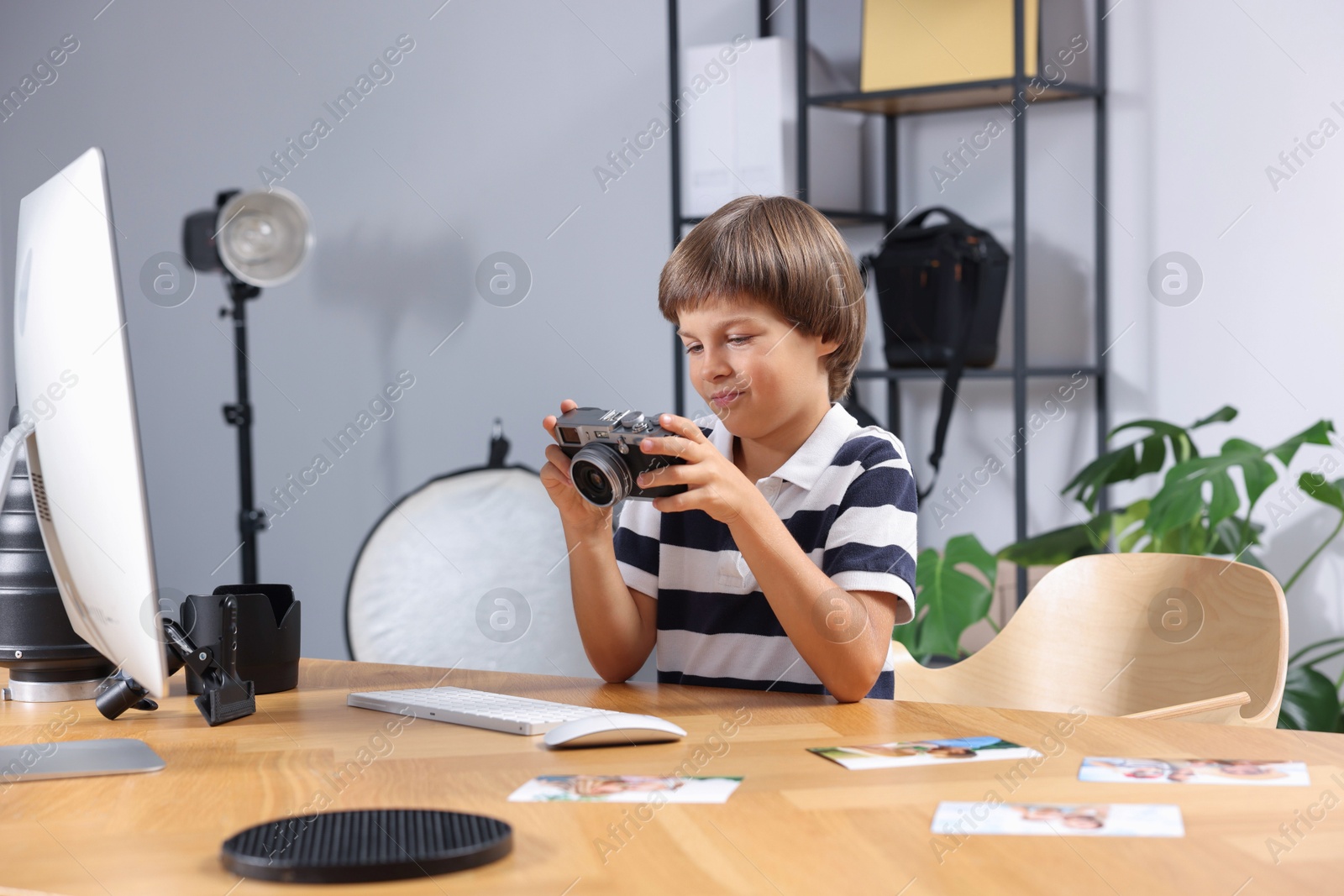 Photo of Choice of profession. Little boy with camera pretending to be photographer at wooden table in studio