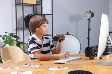 Photo of Choice of profession. Little boy with camera pretending to be photographer at wooden table in studio