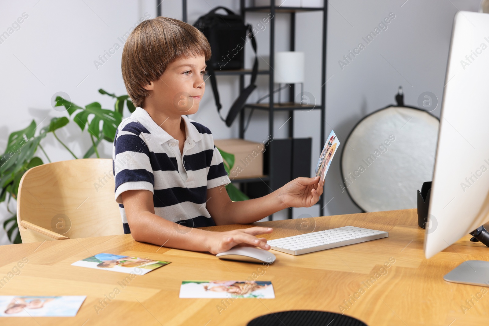 Photo of Choice of profession. Little boy with pictures pretending to be photographer at wooden table in studio