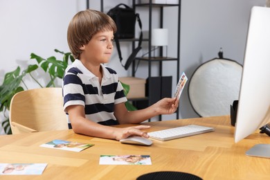 Photo of Choice of profession. Little boy with pictures pretending to be photographer at wooden table in studio