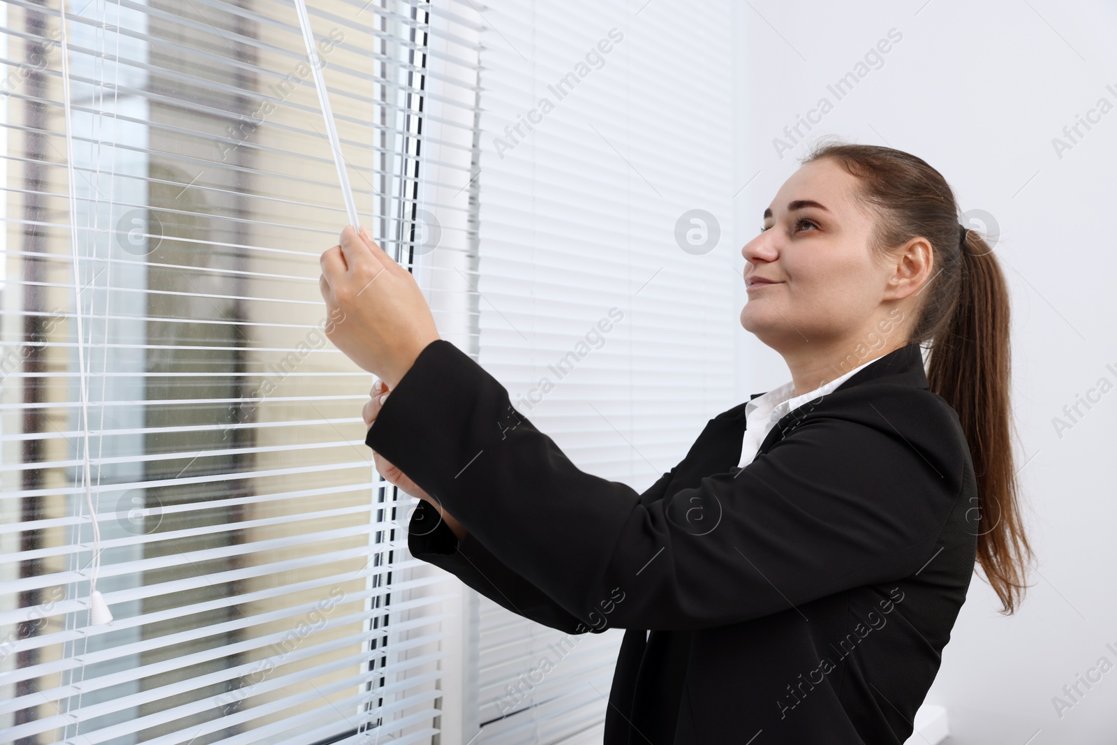 Photo of Woman opening modern window blinds in office
