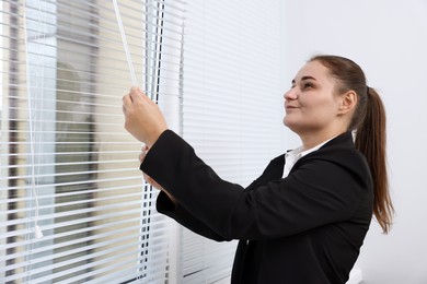 Photo of Woman opening modern window blinds in office