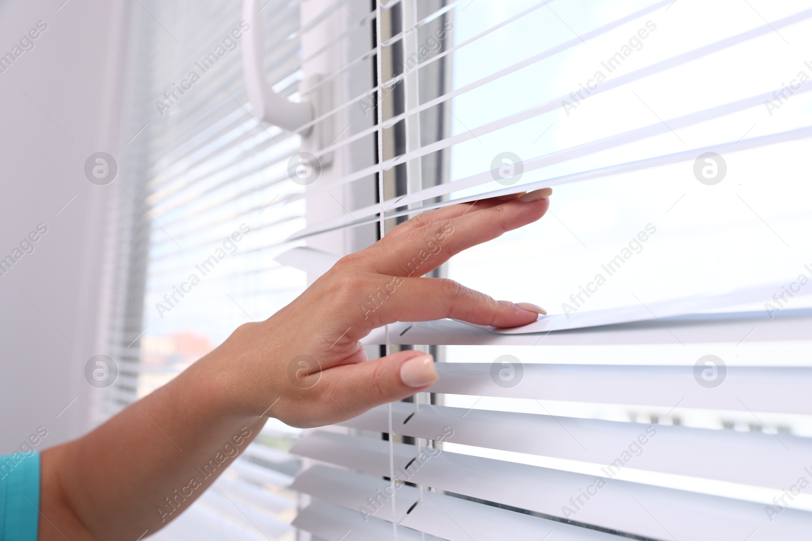 Photo of Woman separating slats of window blinds, closeup